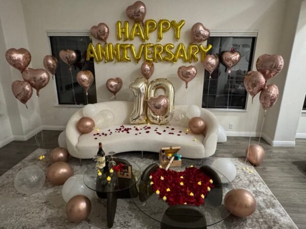 Romantic anniversary room decoration with candles, champagne, heart-shaped rose petals, balloon decor, curated wine, premium chocolate, and keepsake box