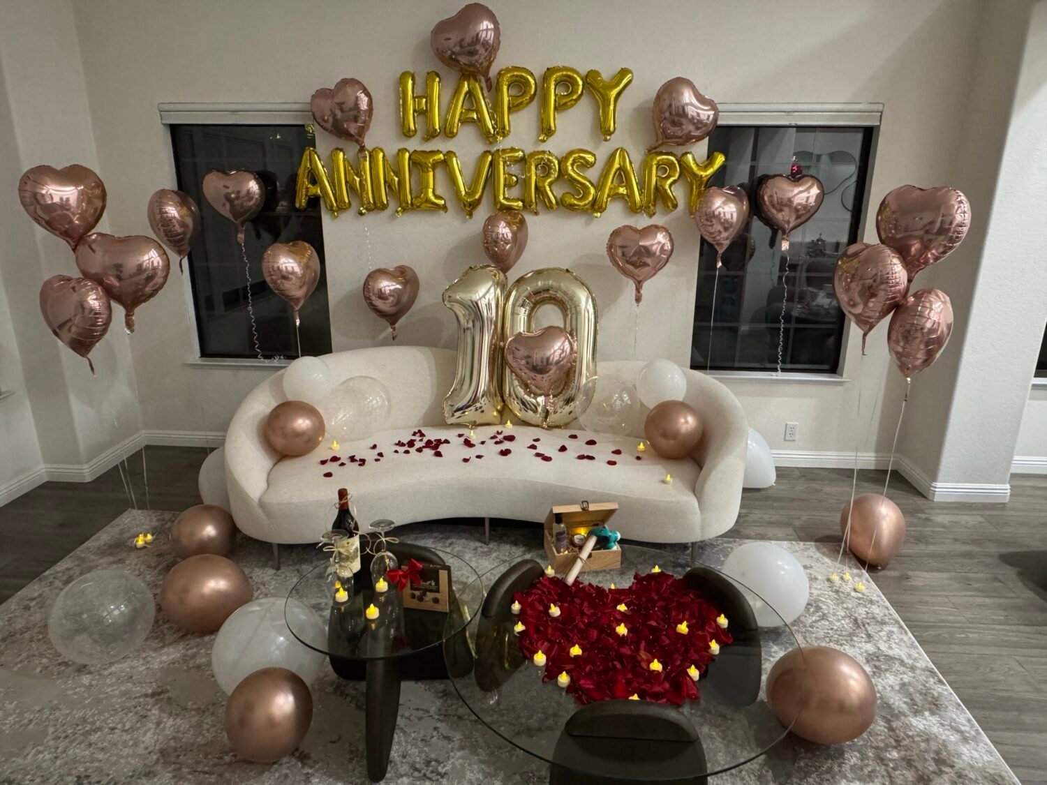 Romantic anniversary room decoration with candles, champagne, heart-shaped rose petals, balloon decor, curated wine, premium chocolate, and keepsake box