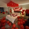 Romantic anniversary room decoration with candles, champagne, heart-shaped rose petals, balloon decor, curated wine, premium chocolate, and keepsake box